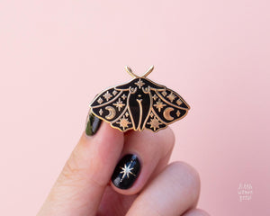 Black and gold enamel pin featuring original feminist artwork of a moth lady. Stars, moon, celestial motifs decorate the moth girl&#39;s wings.