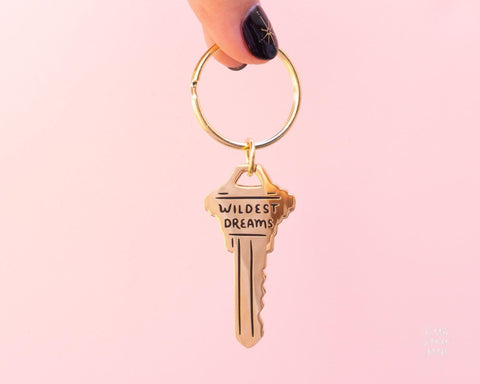 Cute gold metal keychain in the shape of a key with the text &quot; Wildest Dreams&quot; engraved on the key